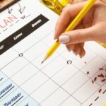 Person holding pencil above a paper for meal planning